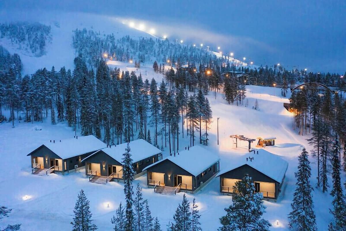 A snow-covered landscape with three cabins, each with a balcony and a staircase leading to the entrance.