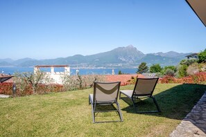 A grassy outdoor area with two chairs facing a scenic view of a coastal town and mountains. - ApartmentsGarda - Albisano Sky House (Torri del Benaco)