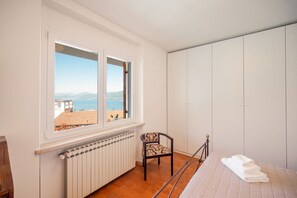A bedroom with a view of the sea, a radiator, a chair, and a bed with towels. - ApartmentsGarda - Albisano Sky House (Torri del Benaco)