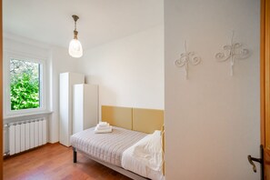 A bedroom with a bed, a radiator, a window with a view of greenery, and a wall-mounted light fixture. - ApartmentsGarda - Albisano Sky House (Torri del Benaco)