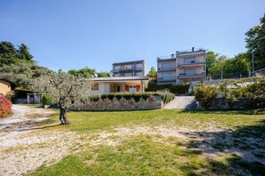 A residential area with a house, a stone wall, and two multi-story buildings in the background. - ApartmentsGarda - Albisano Sky House (Torri del Benaco)