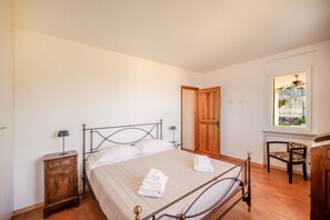 A bedroom with a bed, wooden nightstand, chair, and a window with a view. - ApartmentsGarda - Albisano Sky House (Torri del Benaco)