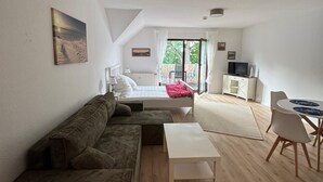 A modern, well-lit room with a large window, a sofa, a small table, and a TV. - Vacation apartment with balcony  (Gustow)