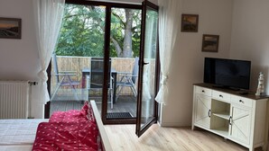 A bedroom with a bed, a TV on a cabinet, a sliding glass door to a balcony, and a view of trees. - Vacation apartment with balcony  (Gustow)