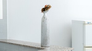 En hvid vase med visne blomster på en granitbordplade foran en hvid væg.
