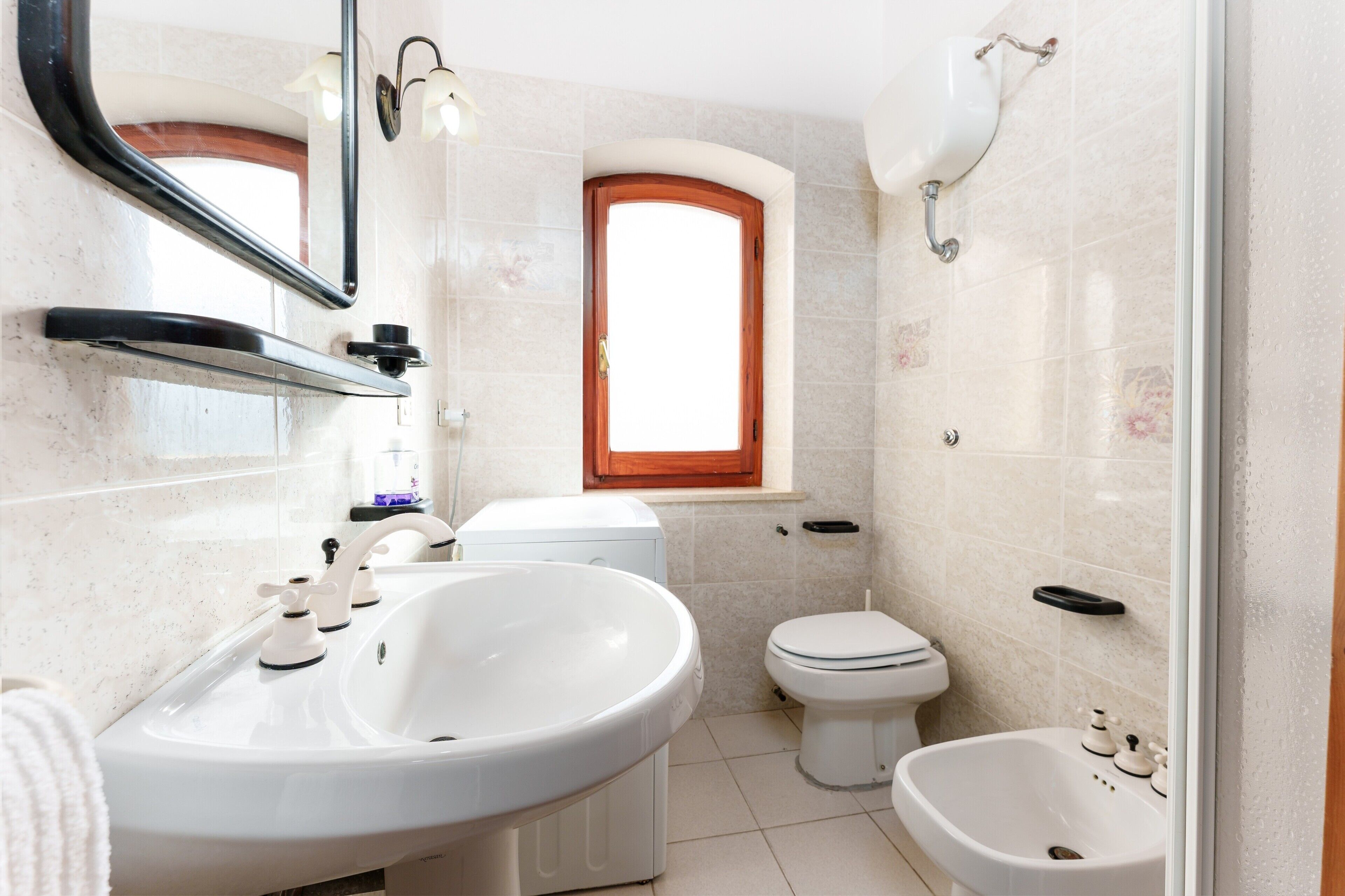 A bathroom with a sink, toilet, bidet, and a window.