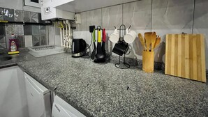 Cozinha com armários brancos, bancada de granito, chaleira, cafeteira e utensílios.