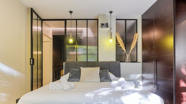 A modern bedroom with a large bed, a bedside table, and a view through a sliding door. - MONTAIGNE EXECUTIVE SUITE (Paris)