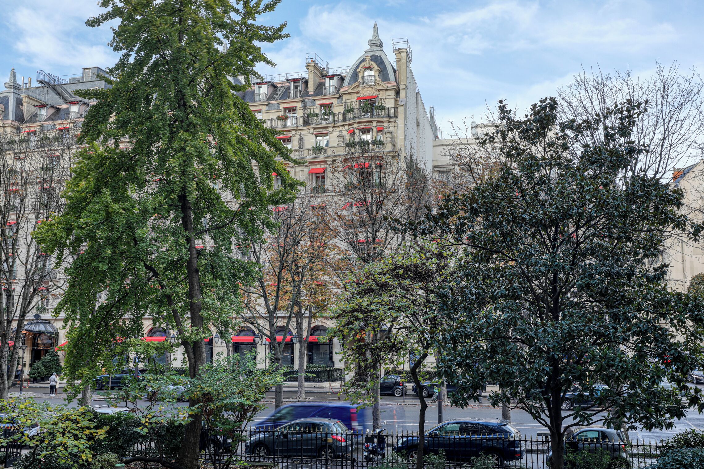 Un edificio de varios pisos con balcones, una calle en frente y árboles.