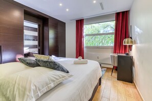 Ein Schlafzimmer mit einem großen Bett, einem Schreibtisch, einem Stuhl und einem Fenster mit Vorhängen.
