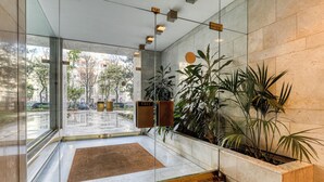 A modern lobby with a glass entrance, a reception desk, and a large potted plant. - MONTAIGNE EXECUTIVE SUITE (Paris)