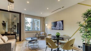 A modern living room with a sofa, chairs, a round table, and a large window. - MONTAIGNE EXECUTIVE SUITE (Paris)