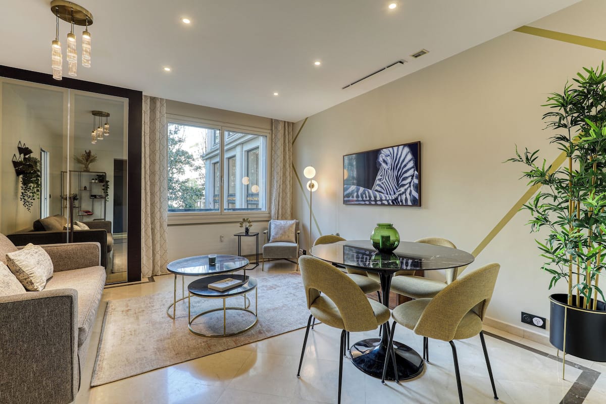 Uma sala de estar moderna com um sofá, cadeiras, uma mesa redonda e uma janela grande.
