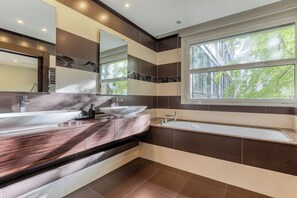 Ein modernes Badezimmer mit einem Doppelwaschtisch, einer Badewanne und einem großen Fenster für natürliches Licht.