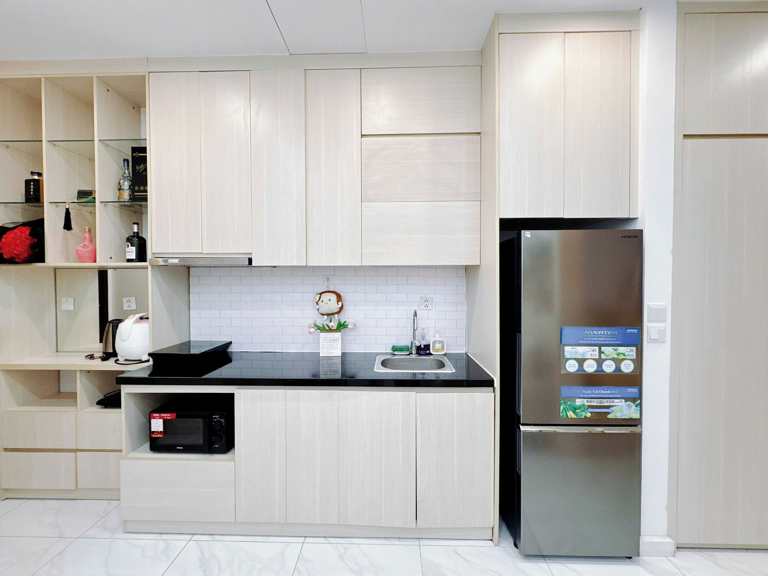 Une cuisine moderne avec des meubles de couleur bois clair, un plan de travail noir, un réfrigérateur en acier inoxydable et un four à micro-ondes.
