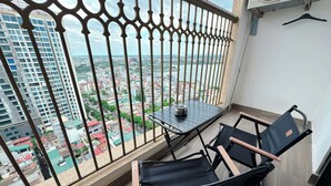 A balcony with a table and two chairs, overlooking a cityscape with buildings and a river.