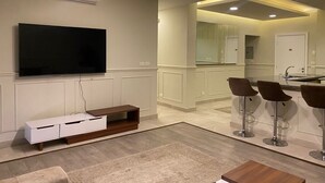 Una sala de estar moderna con un televisor de pantalla plana, un mueble de madera para entretenimiento y una zona de estar con taburetes de bar.
