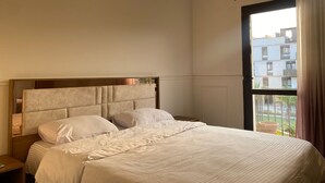 Un dormitorio con una cama grande, cabecera de madera y ventana con vistas a edificios y follaje.