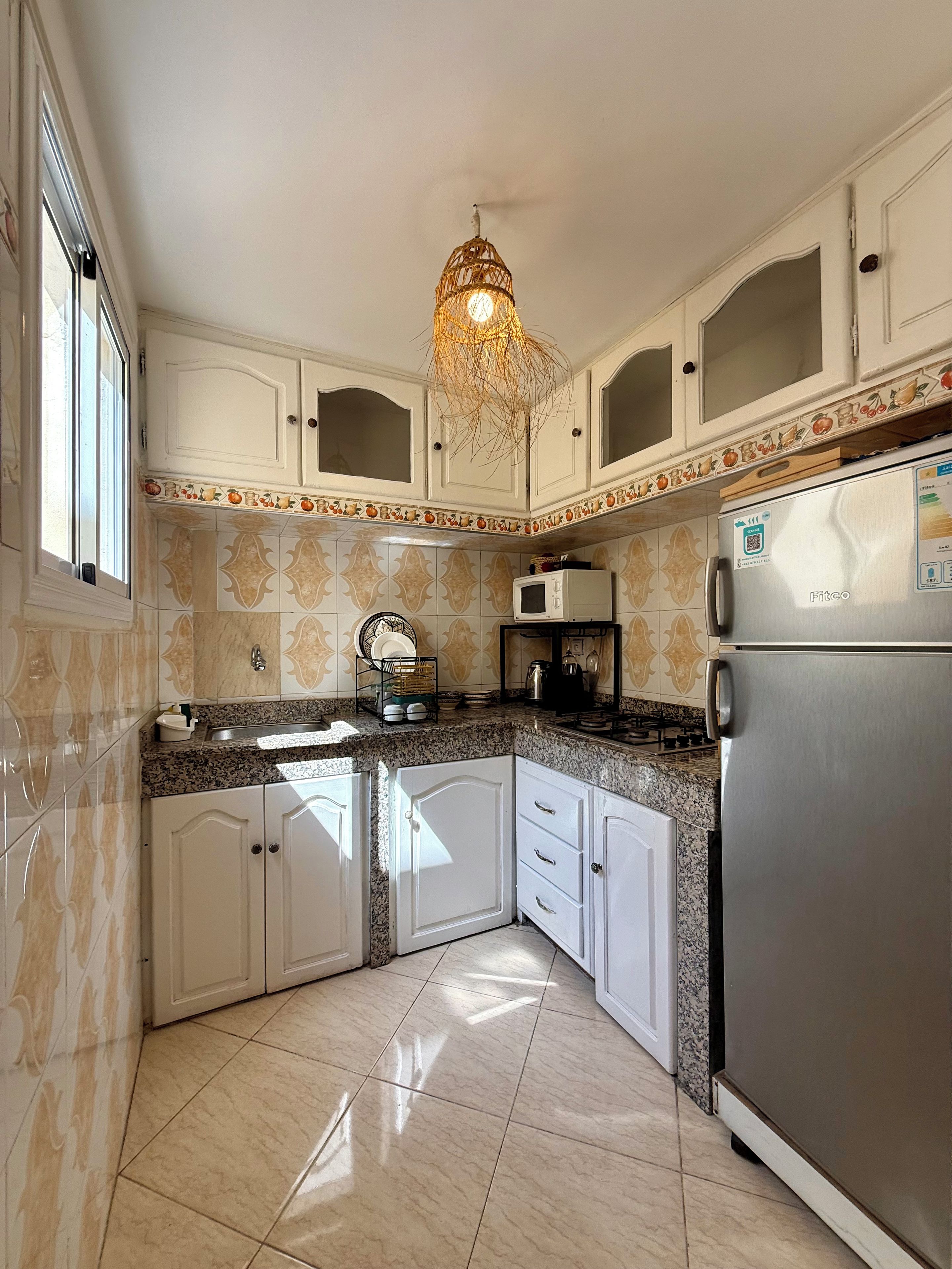 A kitchen with white cabinets, a stainless steel refrigerator, a microwave, and a decorative ceiling light fixture.