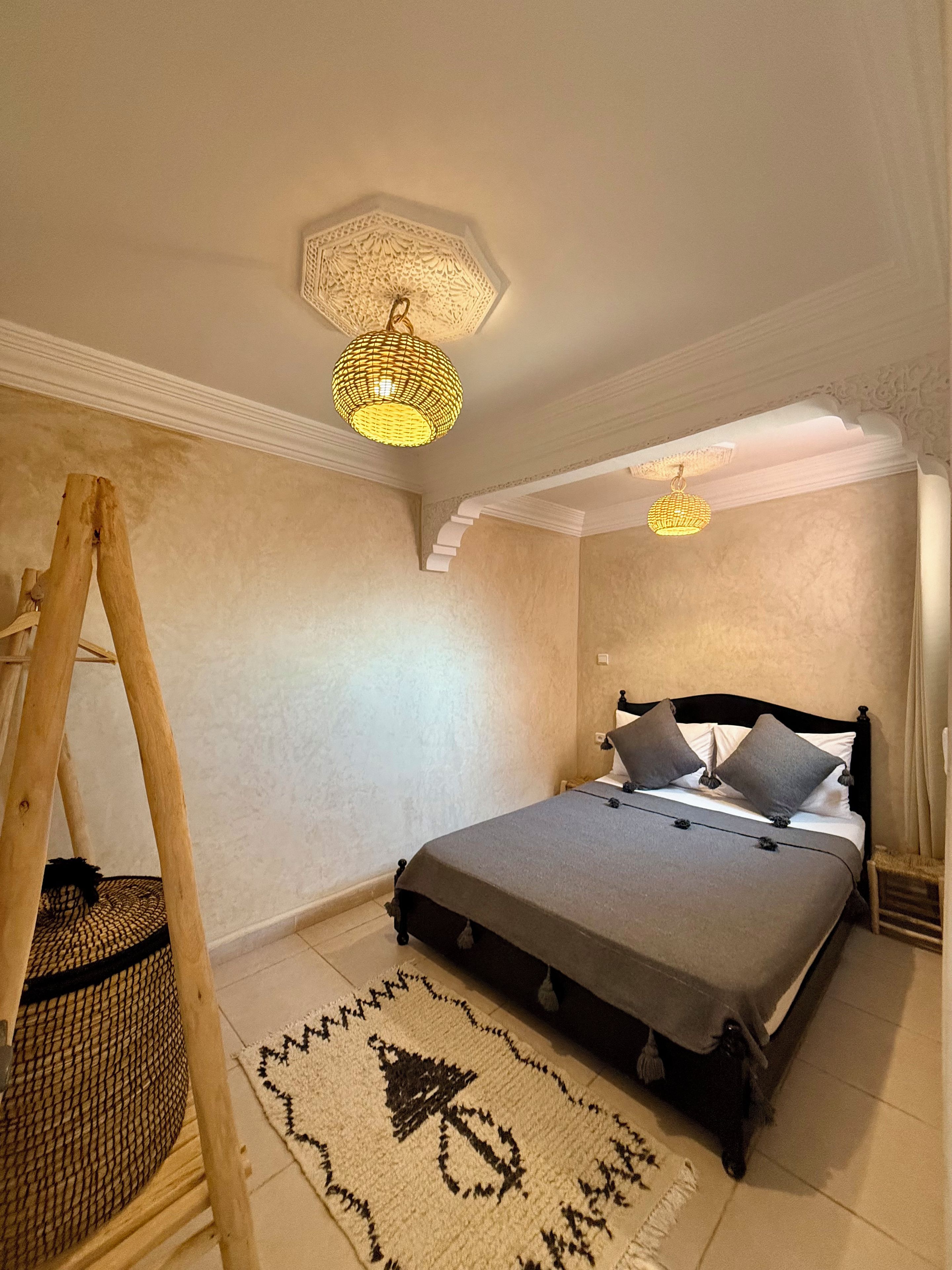 A bedroom with a bed, a wooden ladder, a woven basket, and a patterned rug.