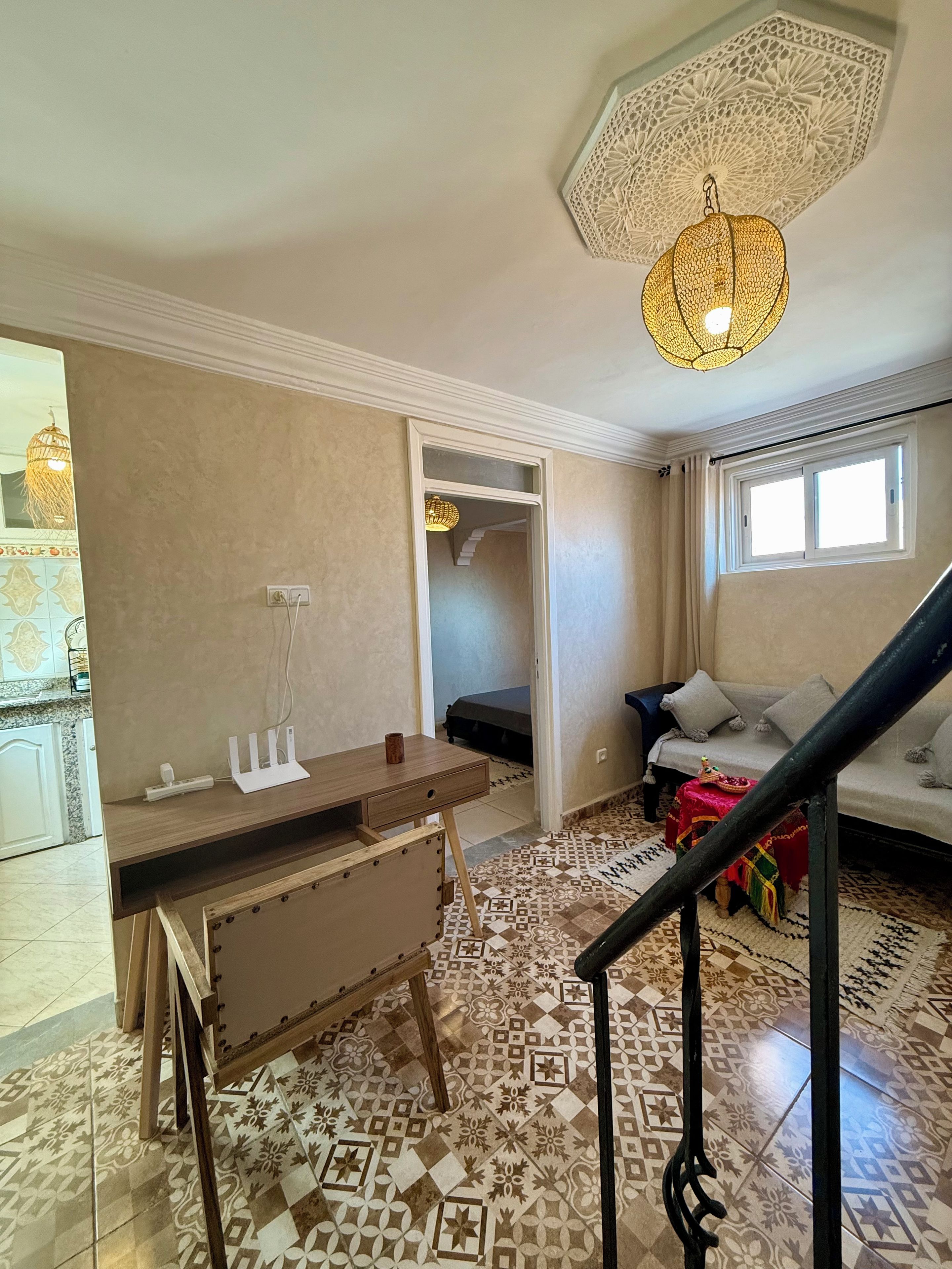 A room with a desk, a bed, a sofa, a staircase, and patterned flooring.
