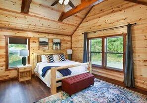 A wooden cabin bedroom with a bed, bench, and large windows. - 8-Bedroom Smoky Mountain Cabin with Indoor Pool, Outdoor Theater & Arcade (Sevierville)