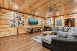 A wooden interior with a sofa, a table, and a ceiling fan. - 8-Bedroom Smoky Mountain Cabin with Indoor Pool, Outdoor Theater & Arcade (Sevierville)