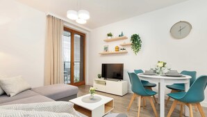 Ett modernt vardagsrum med en soffa, ett soffbord, en tv och en matplats med stolar och ett bord.