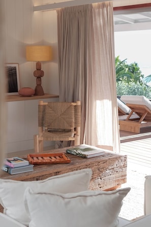 Una habitación con cama, una silla de madera, una mesa con libros y una bandeja, una lámpara y vistas al exterior.