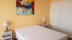 Ein Schlafzimmer mit einem Bett, zwei Nachttischen mit Lampen, einem Kleiderschrank und einem farbenfrohen, abstrakten Gemälde an der Wand.