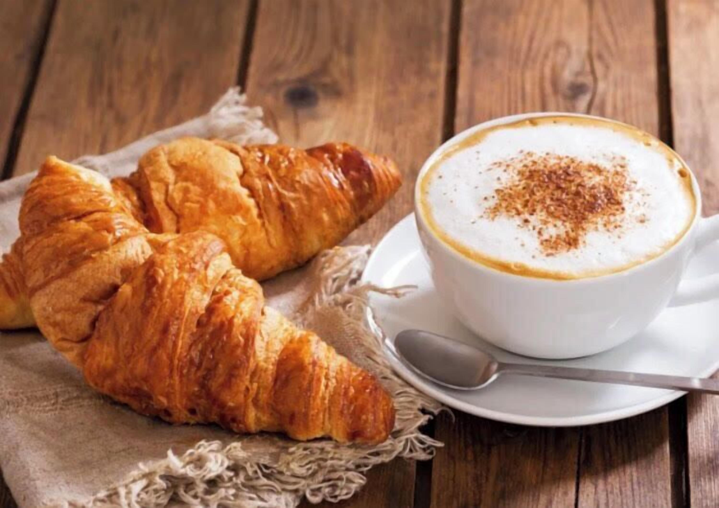 A croissant and a cup of coffee on a wooden table.