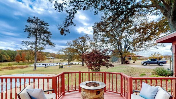 A covered outdoor deck with a stone fire pit, red railings, and two cushioned chairs. - Pool, Fire Pit & Pond: Angler's Retreat in Griffin (Griffin)