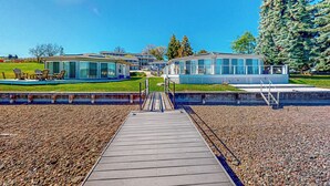 A modern building with a glass facade, a wooden deck, and a landscaped area with grass and trees. - Soft Sunsets & Still Water at Flathead Condo (Polson)