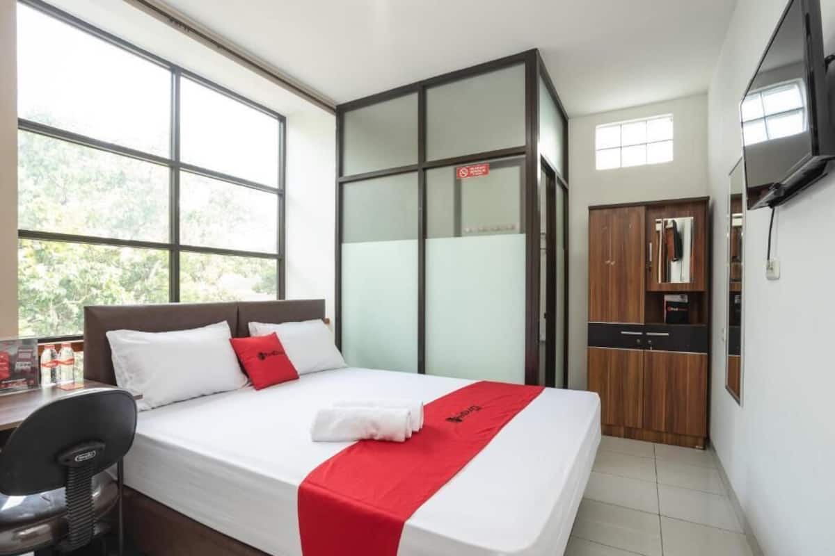 A hotel room with a bed, a desk, a chair, a kitchenette, and a TV.
