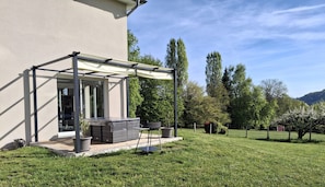 Ein überdachter Außenbereich mit Tisch und Stühlen, einem Blumentopf und einer Pergola.