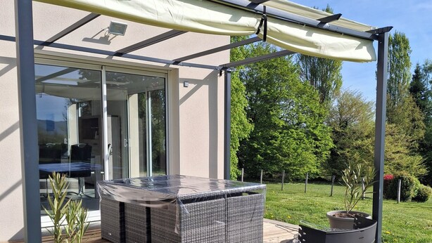 A covered patio area with a seating arrangement, a grill, and a potted plant.