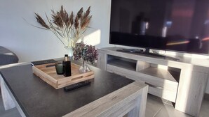 A modern living room with a wooden coffee table, a flat-screen TV on a wooden stand, and a vase with dried plants.