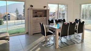 A modern dining area with a glass table and black chairs, large windows offering a view of a snowy landscape, and a wooden cabinet with decorative items.