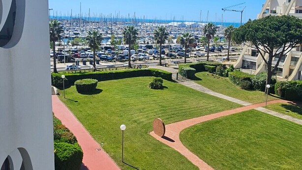 Blick auf eine Marina mit Booten, einem klaren blauen Himmel und einer gepflegten Grünanlage mit Wegen.