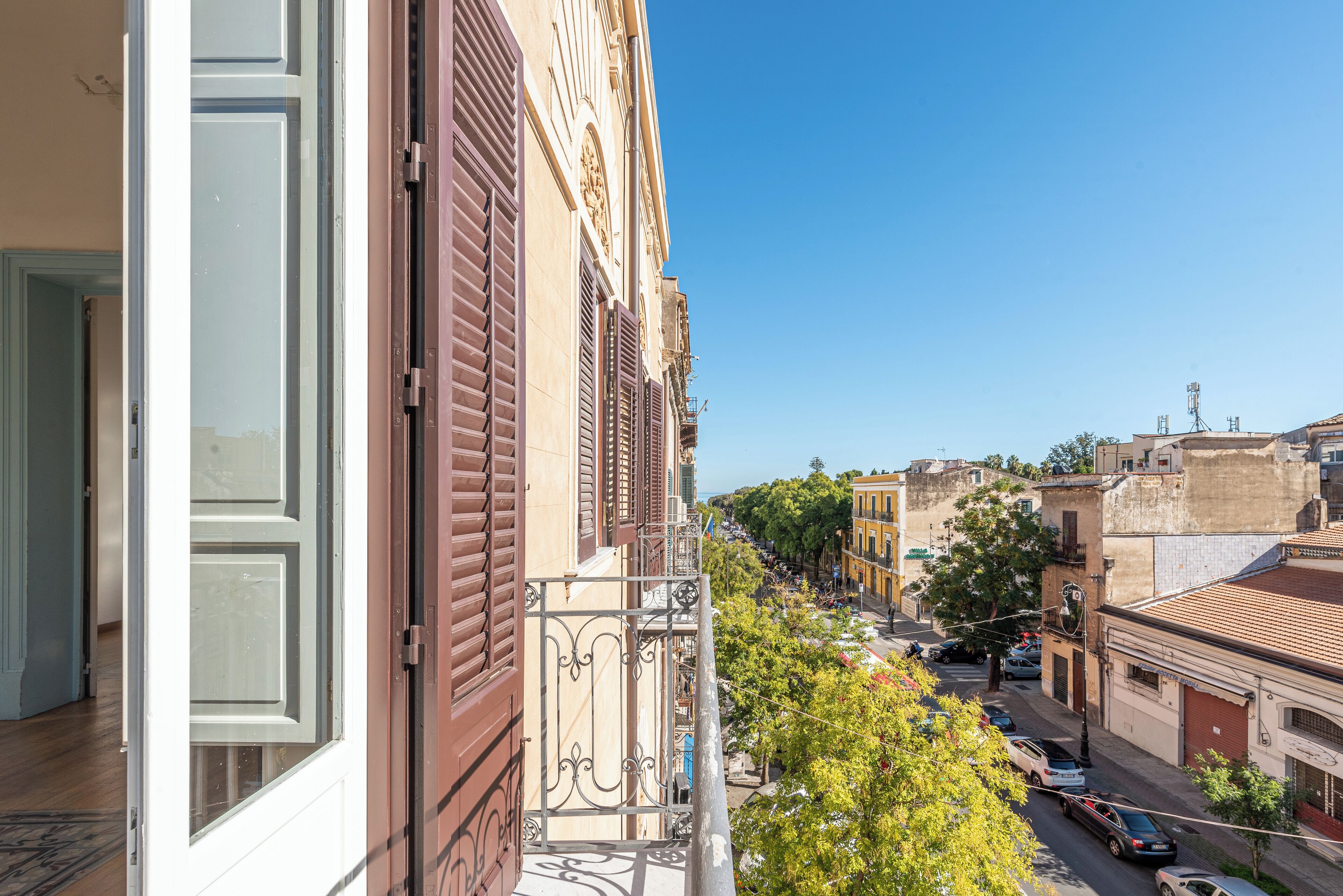 Ein Balkon mit Blick auf eine von Bäumen gesäumte Straße und geparkte Autos.