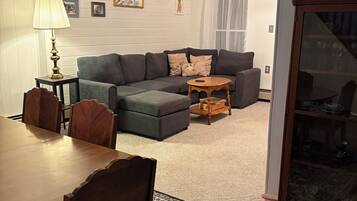 A living room with a sofa set, a dining table with chairs, a lamp, and a patterned rug.