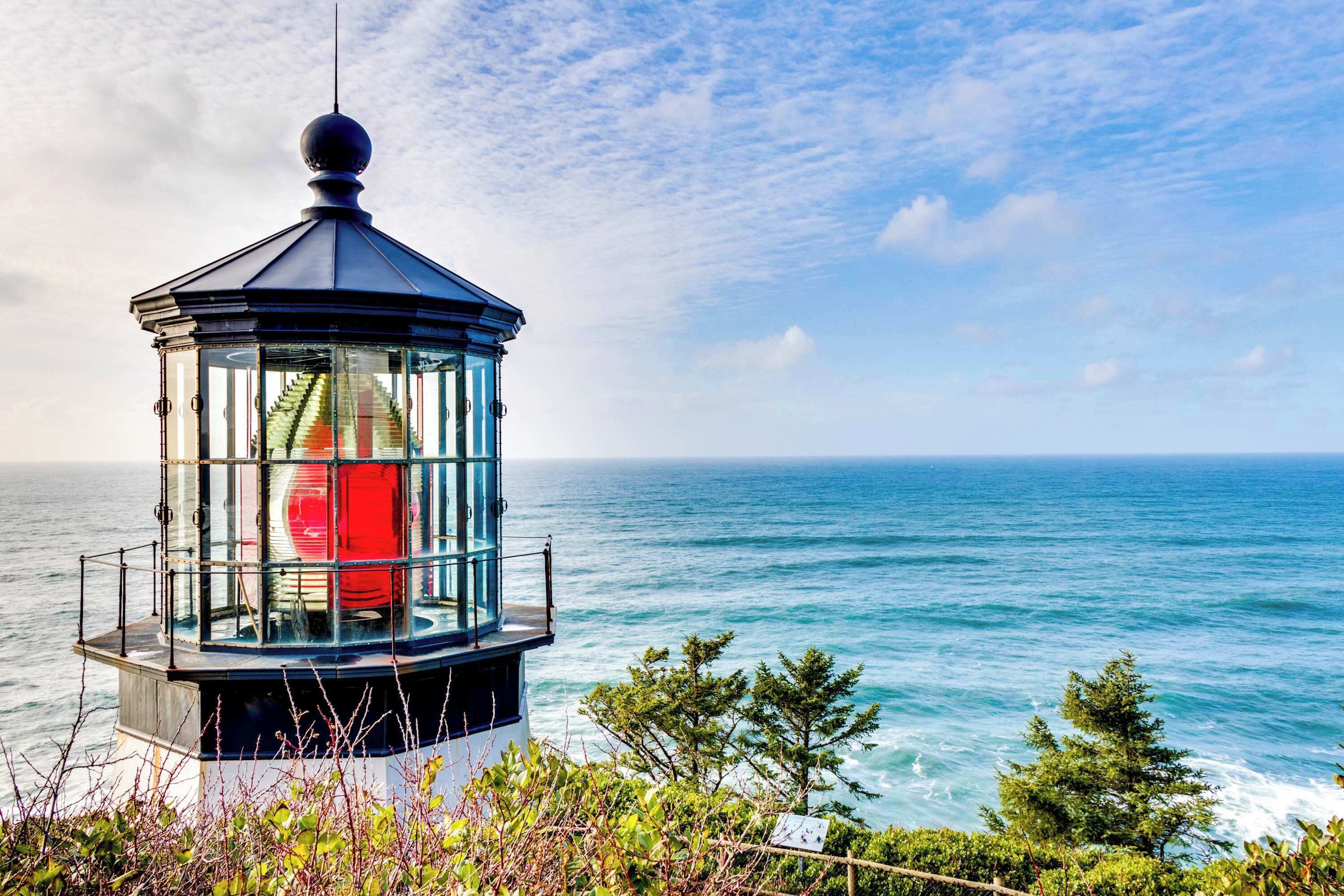 A lighthouse with a glass enclosure, situated on a cliff overlooking the sea.