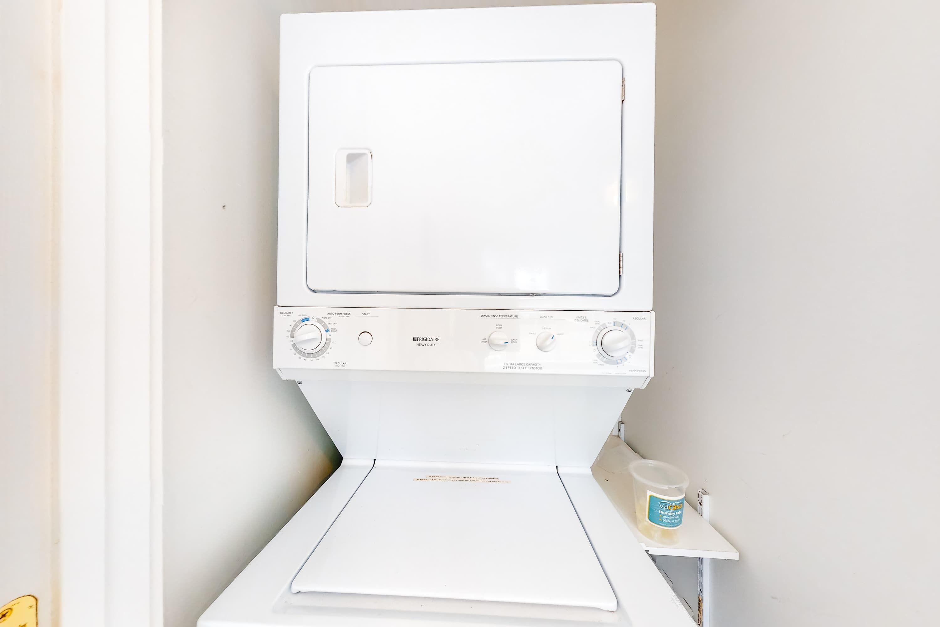 Eine weiße, robuste Waschmaschine und Trockner-Kombination von Frigidaire mit Bedienfeld, Dosierfach und einer kleinen Ablagefläche mit Behälter.
