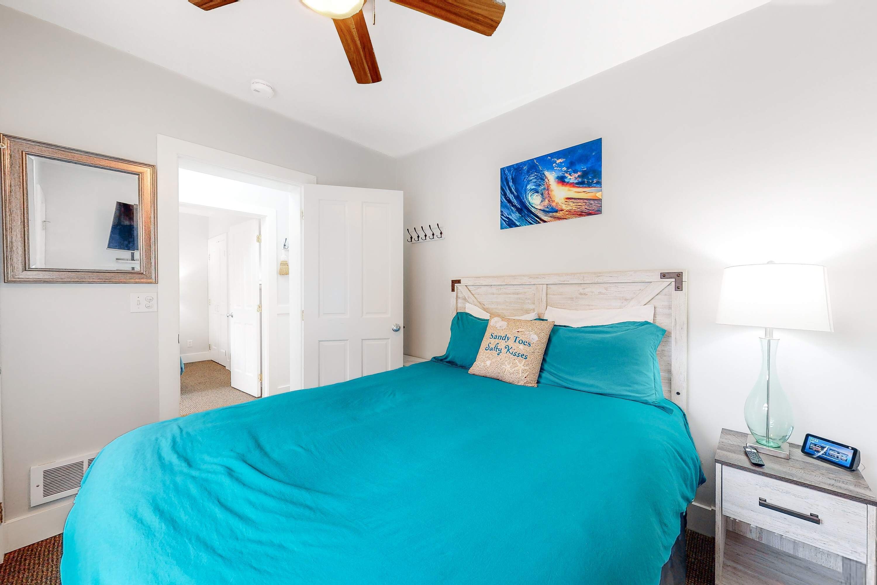 A bedroom with a large bed, a ceiling fan, a nightstand with a lamp, and a painting on the wall.