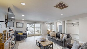 A spacious living room with a large window, a flat-screen TV mounted on the wall, and a dining area with a table and chairs. - Oceanfront dog friendly home with coastal views telescope walkable location (Depoe Bay)