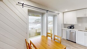 A modern kitchen with white cabinets, a stainless steel dishwasher, and a wooden dining table with chairs. - Oceanfront dog friendly home with coastal views telescope walkable location (Depoe Bay)