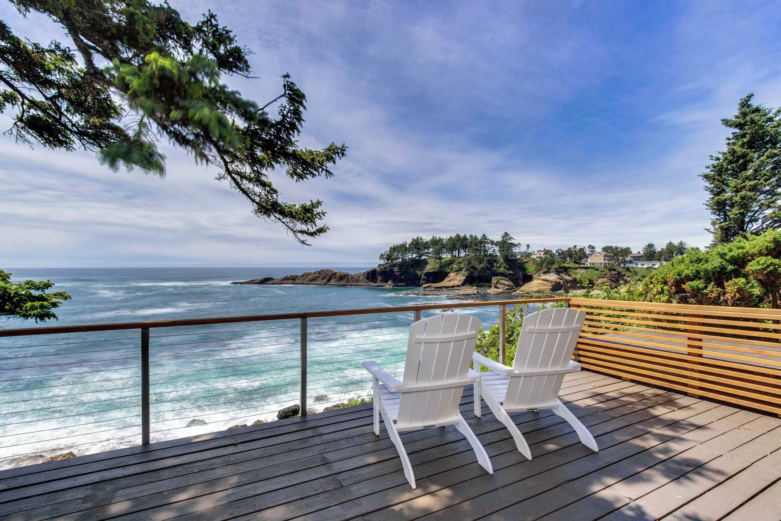 A wooden deck with two white chairs overlooking a coastal view.