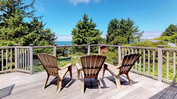 Une terrasse en bois avec trois chaises Adirondack donnant sur un paysage pittoresque composé d’arbres et d’une étendue d’eau.