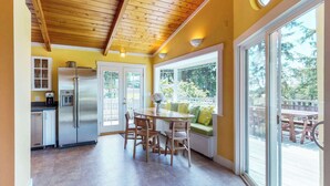 Une cuisine avec un plafond en bois, un réfrigérateur en acier inoxydable et un coin repas comprenant des chaises et une table en bois.