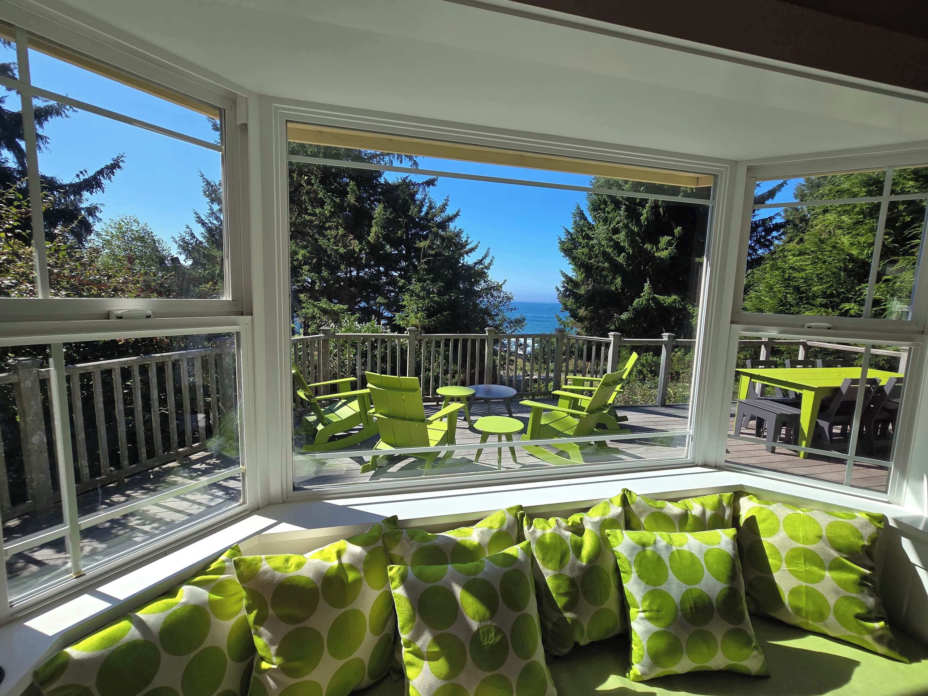 A sunlit room with a view of the ocean, green chairs, and a table.